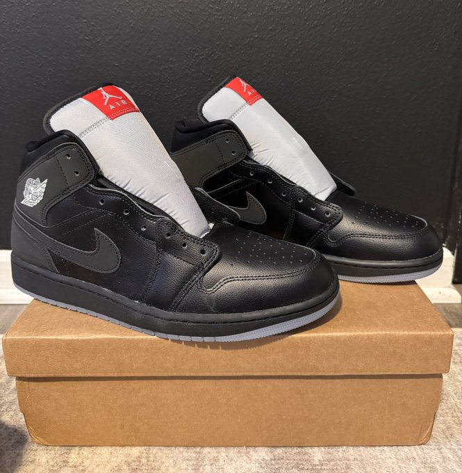 A pair of black and white high-top sneakers, likely Air Jordan 1s, resting on a brown cardboard shoebox.