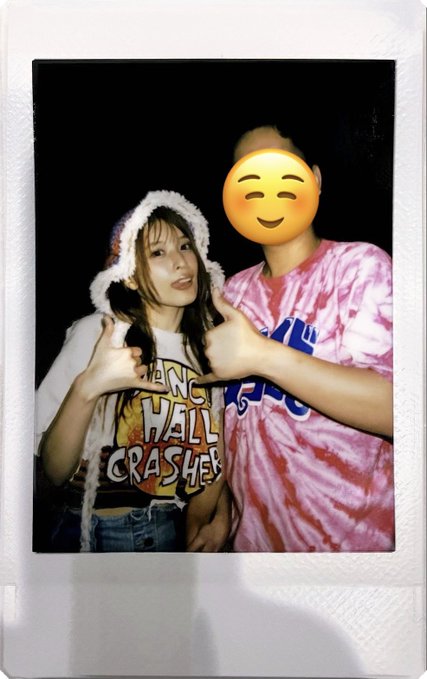 A Polaroid-style photo of two young women, one with face obscured by an emoji, both wearing tie-dye shirts and making finger-gun gestures toward the camera.