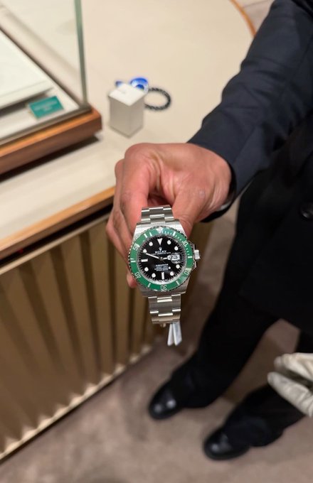 A hand holds up a silver Rolex Submariner watch with a green bezel.