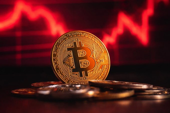 Bitcoin coins in the foreground with a red downward trending stock chart line in the background.