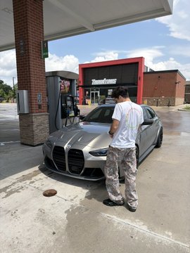 A man fuels up a gray BMW M3 Competition xDrive at a gas station, with the "TradeZone" business sign visible behind him, celebrating his achievement of buying his dream car cash after transitioning from a Target job to full-time trading profits.