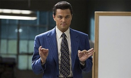 Leonardo DiCaprio as Jordan Belfort in a blue pinstripe suit and patterned tie, gesturing with his hands in what appears to be a scene from The Wolf of Wall Street.