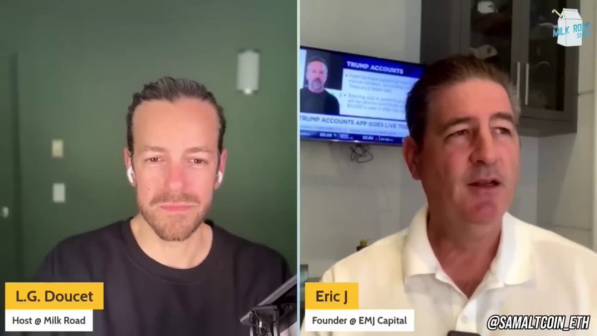 The image shows two men sitting next to each other, with one man wearing a black shirt and the other wearing a white shirt. They are both looking at a TV screen that displays an interview between Eric Jackson of EMJ Capital and another person. The TV is positioned in front of them, and they appear to be engaged in conversation or discussing something on the screen.