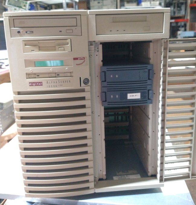 A vintage Digital AlphaServer 1000A computer tower with its side panel removed, revealing internal drive bays on a workshop table.