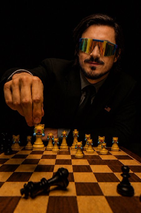 A man in a black suit and reflective visor sunglasses smirks while reaching for the final white king piece on a chessboard, with a black piece toppled in the foreground—visually framing a "checkmate" moment. The image serves as a metaphor for $MOG dominating the board, suggesting it's about to make its winning move toward a listing.