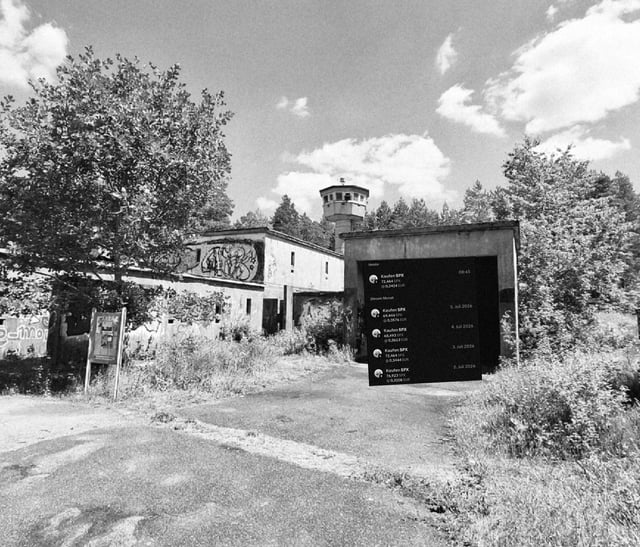 A black and white photograph of an abandoned building with a watchtower, overgrown vegetation, and a small dark overlay showing what appears to be a comments or followers list interface.
