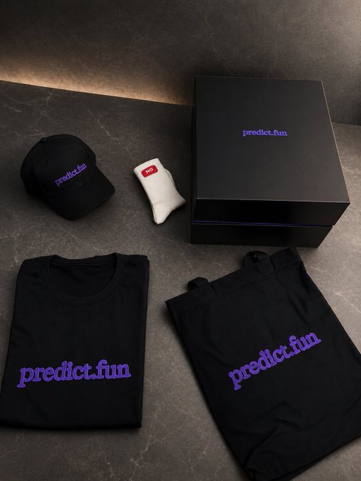 A flat lay display of 'predict.fun' branded merchandise including a black cap, t-shirt, tote bag, and gift box alongside a white sock with a '100' emoji.