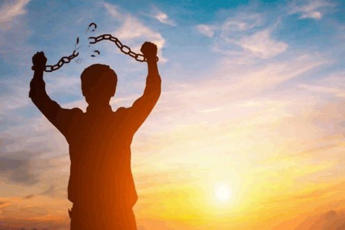 A silhouette of a man breaks free from chains with his arms raised against a bright sunset sky.