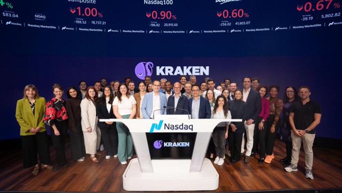 A group photo of the Kraken team at the Nasdaq stock exchange, with the Kraken logo displayed on screen behind the podium.