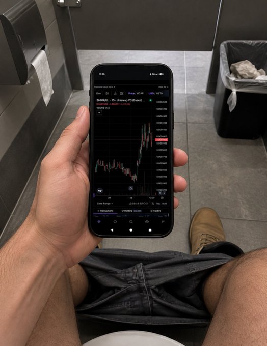 A first-person view of someone sitting in a bathroom holding a smartphone displaying a crypto trading chart for BNK/UD, showing a candlestick price graph.