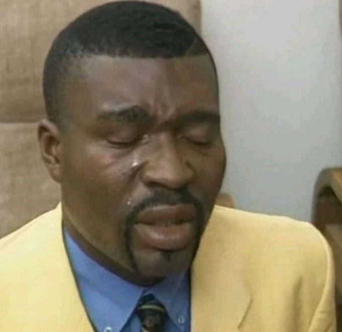 A close-up of a man with a short beard wearing a yellow suit jacket over a blue shirt, with tears visibly on his face.