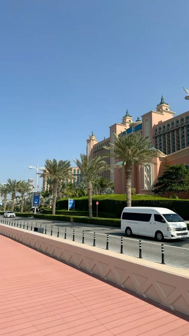 A view of the Atlantis The Palm hotel in Dubai with its distinctive pink architecture, framed by palm trees and a white van driving on the road.