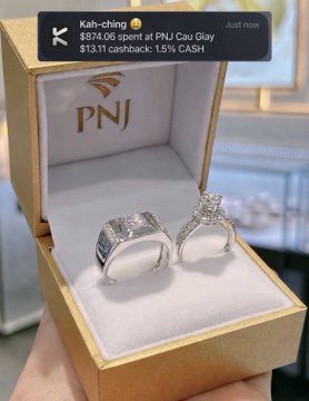 The image shows two engagement rings placed inside a gold jewelry box with a gold background. The person holding the box has just made a purchase from PNJ and received a cashback notification via text message.