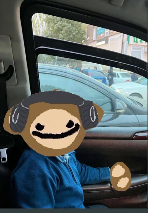 A child in a blue zip-up jacket sits in the back seat of a car looking out the window, with their face obscured by a doodled emoji sticker.