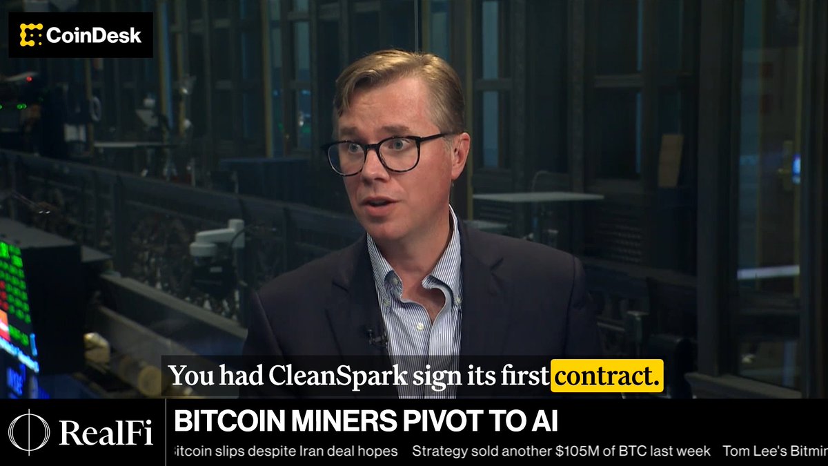 A CoinDesk video interview with a man wearing glasses and a blue shirt in front of a screen displaying financial data, with the RealFi logo visible. The on-screen text reads 'BITCOIN MINERS PIVOT TO AI' and 'You had CleanSpark sign its first contract.'