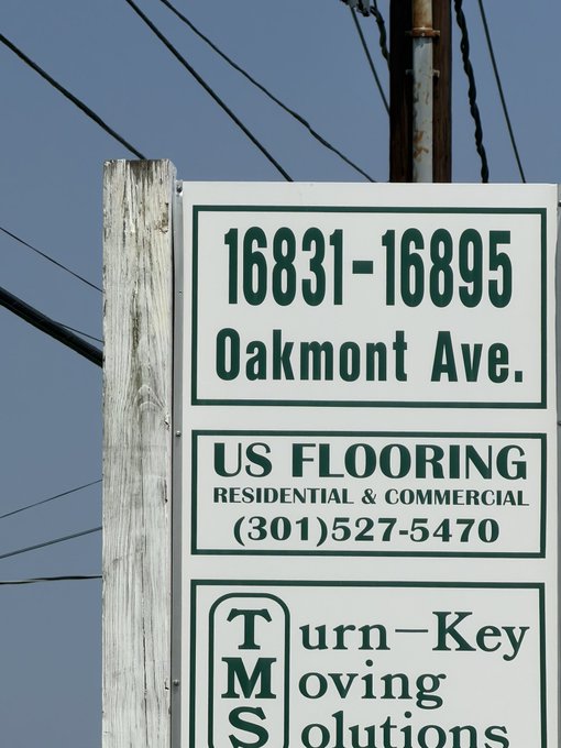 A street sign at 16831-16895 Oakmont Ave. stands against a blue sky, advertising US Flooring at (301)527-5470 and Turn-Key Moving Solutions—fitting for the caption "I'm on the winning block today," as Oakmont is famously associated with the U.S. Open golf tournament.