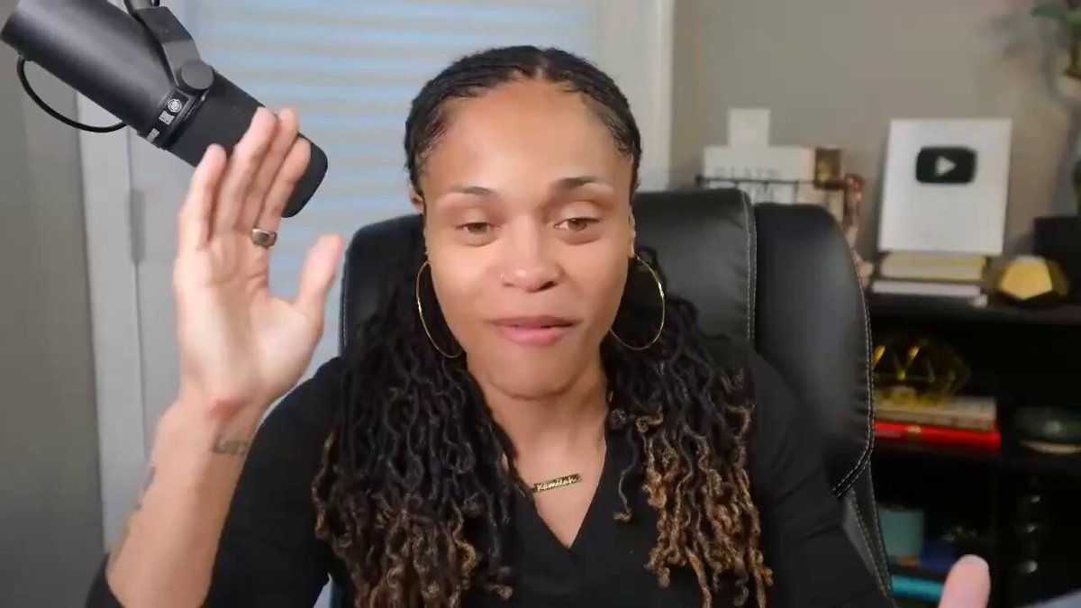 The image shows a woman with long dreadlocks wearing a black shirt, sitting in an office chair while holding a microphone up to her head. The background of the image features a bookshelf filled with various items such as books and vases. There is also a TV visible in the scene. The content of the post seems to be related to cryptocurrency or investing in it, as indicated by the phrase "Focus on what is in the image and how it relates to the post".