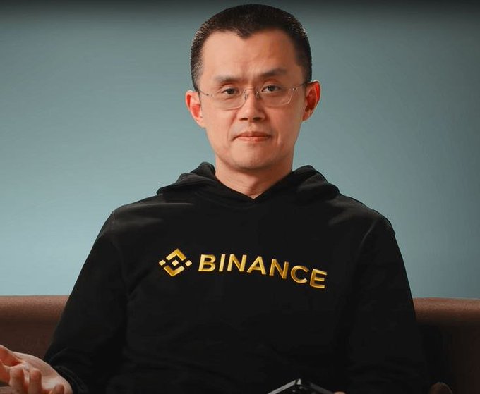 A man wearing a black "BINANCE" hoodie sits on a couch against a muted blue background, paired with a post celebrating his multi-billion dollar contrarian crypto investments made during a market downturn.