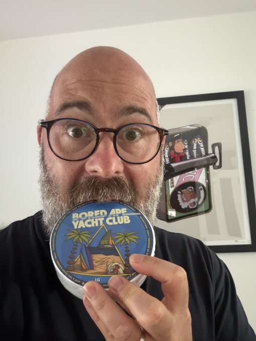 A bald man with glasses holds up a tin of 'BORED APE YACHT CLUB' snus close to his face in what appears to be a product review video.