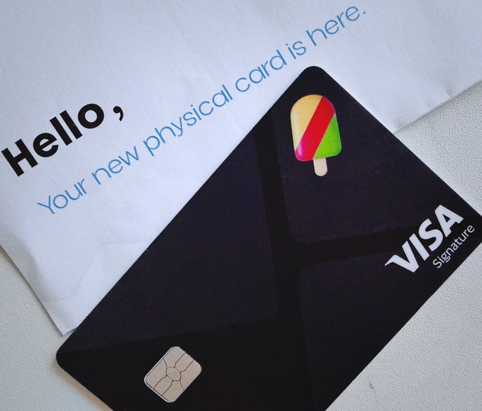 A black Visa Signature card with a popsicle logo rests on a note that reads "Hello, Your new physical card is here."