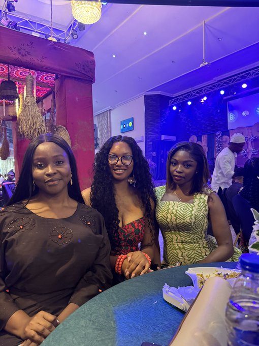 Three smiling young women posing together indoors at what appears to be a restaurant or lounge with decorative purple lighting.