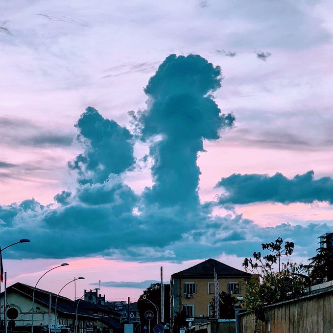 A pink and purple sunset sky over a residential area, featuring a large, dramatic cumulus cloud formation that resembles an exclamation mark or a towering figure.