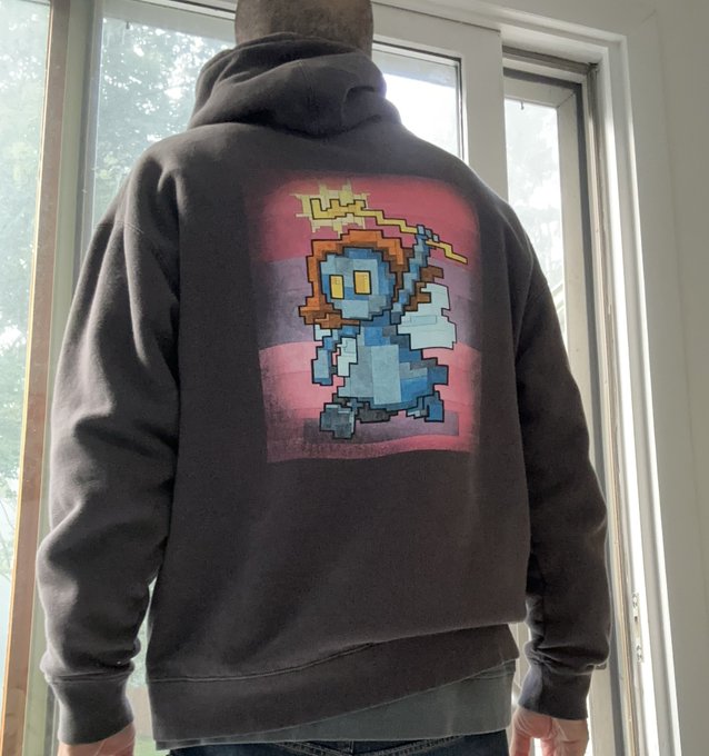 A back view of a person wearing a faded black hoodie featuring a pixel art graphic of a blue wizard character casting a yellow lightning spell against a red and purple gradient background.
