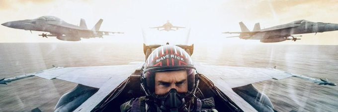 A movie scene from Top Gun: Maverick showing a pilot in the cockpit with 'MAVERICK' on his helmet, flying alongside other fighter jets in formation.