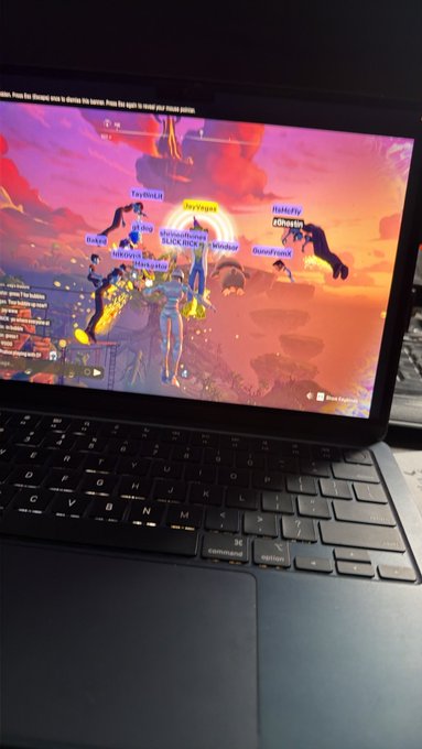 A laptop screen displays a video game scene with warm orange and pink tones, showing multiple player usernames such as "ToyHitLR," "deerayal," and "HuluFlyz" above characters in a desert-like environment.
