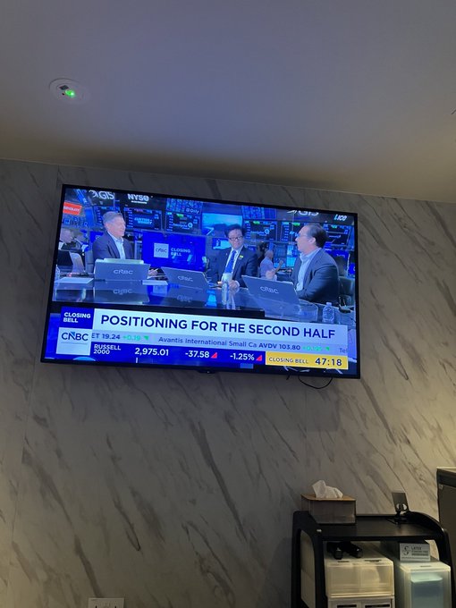 A wall-mounted TV in a marble-walled room displaying a CNBC Closing Bell broadcast titled 'POSITIONING FOR THE SECOND HALF', showing Russell 2000 at 2,973.01 (-37.58) and Awantix International Small Co AWDV 103.60 (-1.25%).