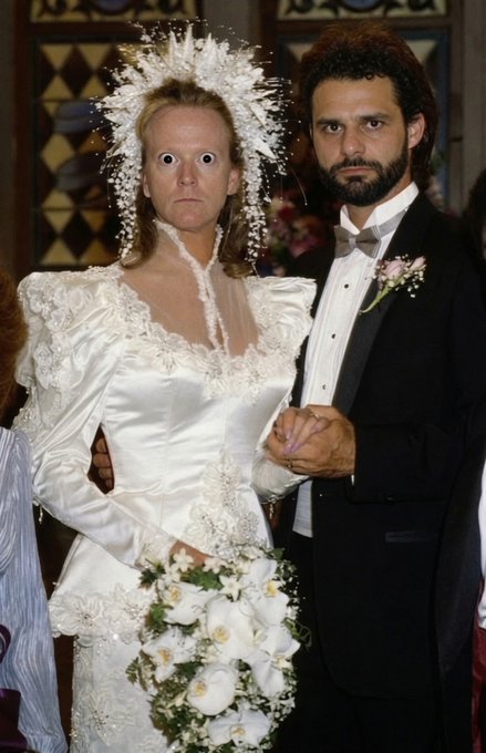 A wide-eyed bride in an elaborate white gown with a sparkling headpiece and bouquet stands beside a bearded groom in a black tuxedo with a boutonnière, both sharing exaggerated, comical facial expressions that match the celebratory yet humorous tone of the "Grand Day $COPE" caption.