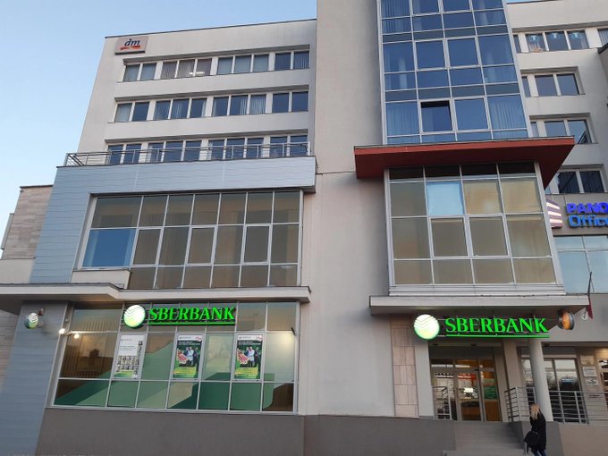 Exterior photograph of a multi-story commercial building featuring Sberbank branches on the ground floor, with a dm store visible on an upper level.