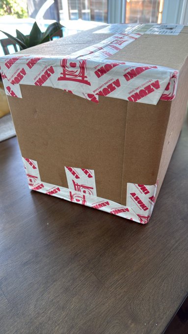 A brown cardboard shipping box sealed with white and red 'LITITY' branded tape sits on a wooden table.