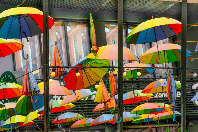 A colorful outdoor installation featuring numerous brightly colored umbrellas and string lights suspended in the air above a street.