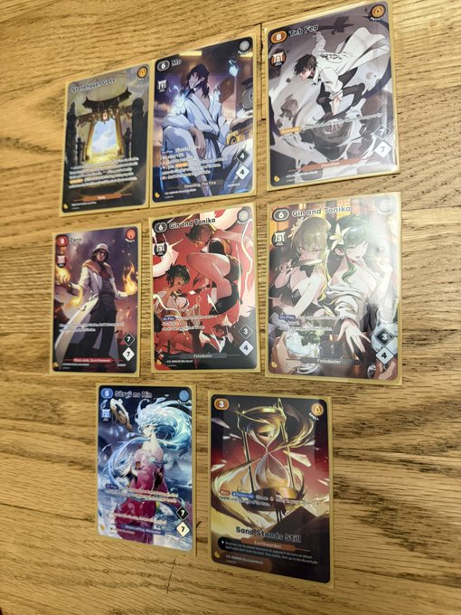 A collection of eight anime-style trading cards laid out on a wooden surface, featuring various character illustrations with titles like 'Saber,' 'Uta and Tanjiro,' and 'Sandalphon: Smite.'