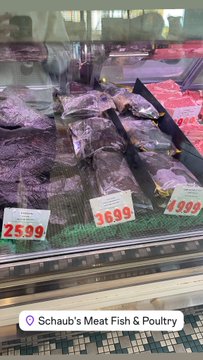 A refrigerated display case at "Schaub's Meat Fish & Poultry" shows packaged cuts of red meat with price tags reading $25.99, $36.99, and $48.99.