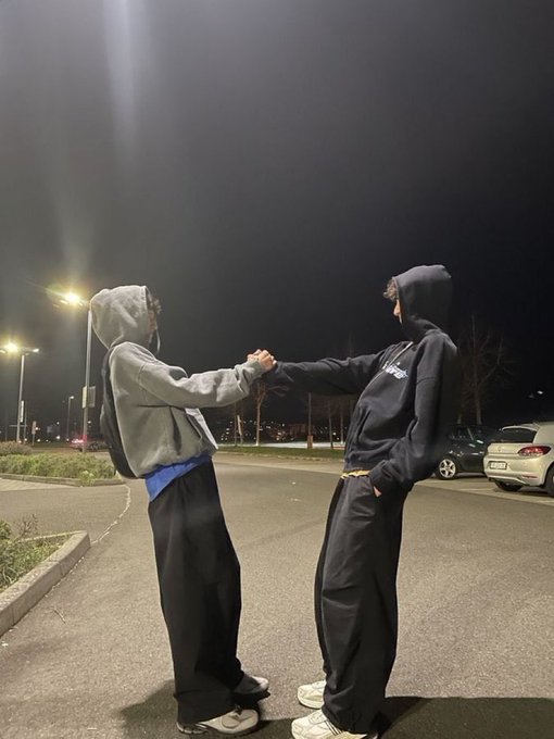 Nighttime photo of two people in hoodies fist-bumping on a street illuminated by streetlights.