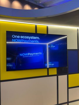 The ChangeNOW x NOWPayments booth features a striking Mondrian-inspired yellow and white wall design with digital displays showcasing the "One ecosystem. NOWPayments" branding. The modern installation aligns perfectly with the post's announcement of the joint booth presence at #TOKEN2049, inviting attendees to stop by and discuss crypto payments with the team.