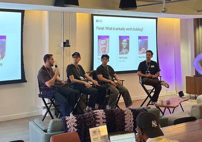 A panel discussion titled 'What is actually worth building?' at a CoinMarketCap event, featuring speakers Doug, Will Nuelle, and Max Wo.