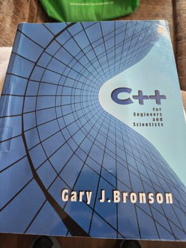 The image features a book titled "C++ for Engineers" by Gary J. Bronson, which appears to be a textbook or guidebook related to programming languages like C++. The book cover has a blue background with a spiral design on it, giving it an interesting and eye-catching appearance.