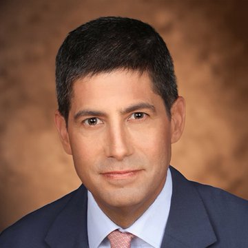 A professional headshot of a man with dark hair wearing a navy suit and tie, shown against a brown studio backdrop. The image appears to be a stock-style portrait, likely representing a financial analyst or commentator sharing the bullish CPI-driven crypto outlook, particularly favorable for Solana (#SOL).