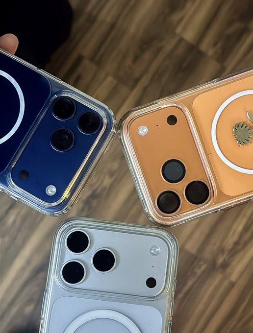 Three iPhones in clear cases—blue, orange/tan with an Apple logo visible on the back, and white—rest on a wooden surface, symbolizing the yearly upgrades referenced in the post's calculation about the opportunity cost of buying new iPhones instead of investing in Bitcoin, Apple stock, or the S&P.