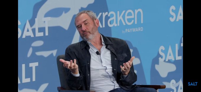 A man with a gray beard speaking at a conference, gesturing with both hands, with 'SALT' and 'Kraken by PAYWARD' logos on the blue backdrop behind him.