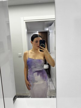 A mirror selfie of a woman wearing a purple and white strapless dress, holding a black smartphone.