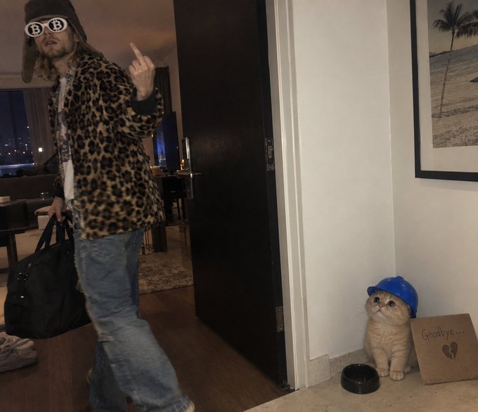 A man in a leopard-print jacket, fur hat, and sunglasses flips off the camera while carrying a black duffel bag, while a small orange cat wearing a blue hard hat sits by a door next to a cardboard sign reading "Goodbye...🖤" and an empty food bowl.

The image humorously illustrates the post's theme of frustration and "goodbye" to someone allegedly ignoring the $BASECAT community, using the dejected cat in a hard hat as a mascot for the abandoned fanbase.