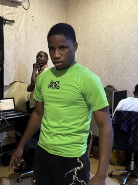 A young man poses confidently in a bright green "Hack Hustle" t-shirt in what appears to be a workspace or office setting, ready to take on the hackathon challenge mentioned in the post. Other people and computer equipment are visible in the background, suggesting a collaborative tech environment.