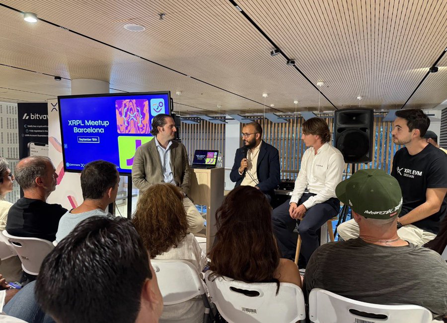 A panel discussion at the XRPL Meetup Barcelona on September 18th, with four speakers seated in front of an attentive audience, sponsored by bitvavo and Commons XR, featuring a company representative in an XPRELEVN Blockchain t-shirt.