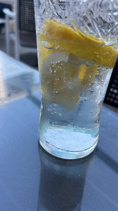 A tall glass filled with ice and lemon slices sits on a blue table, with what appears to be a tissue nearby.