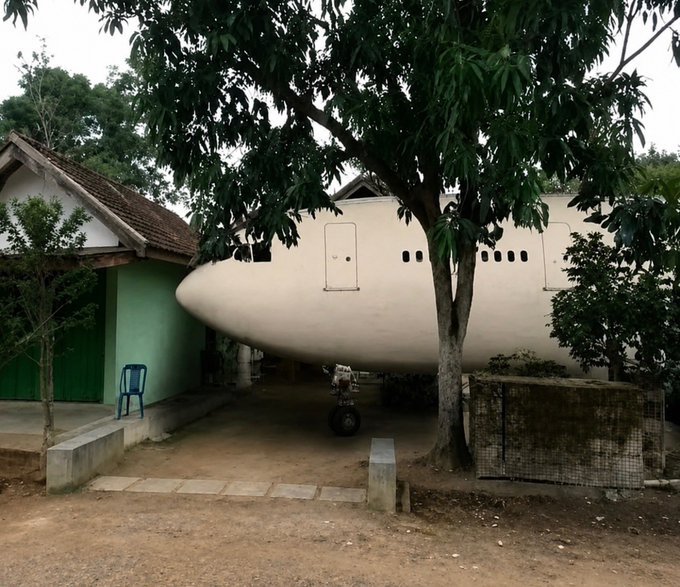 An abandoned airplane fuselage sitting next to a small house among trees.