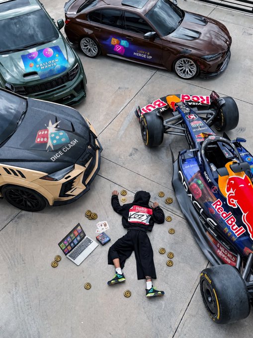 An aerial view shows a person lying on the ground surrounded by luxury and racing vehicles branded with 'Dice Clash,' 'Merge Up,' and 'Red Bull,' along with scattered gold coins and a laptop.